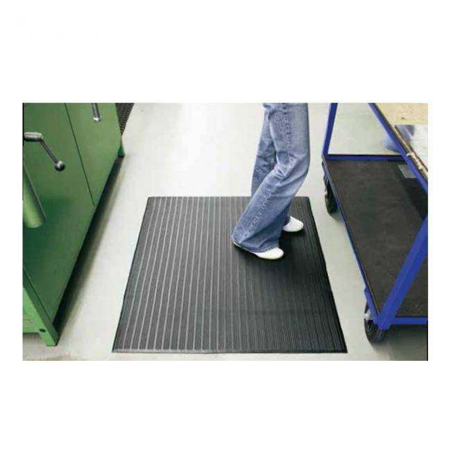 Arbeitsplatzmatte 'SANO' aus Vinylschaum mit rutschhemmender Rippen-Oberfläche vor Werkbank im Büro- oder Werkstattbereich platziert.