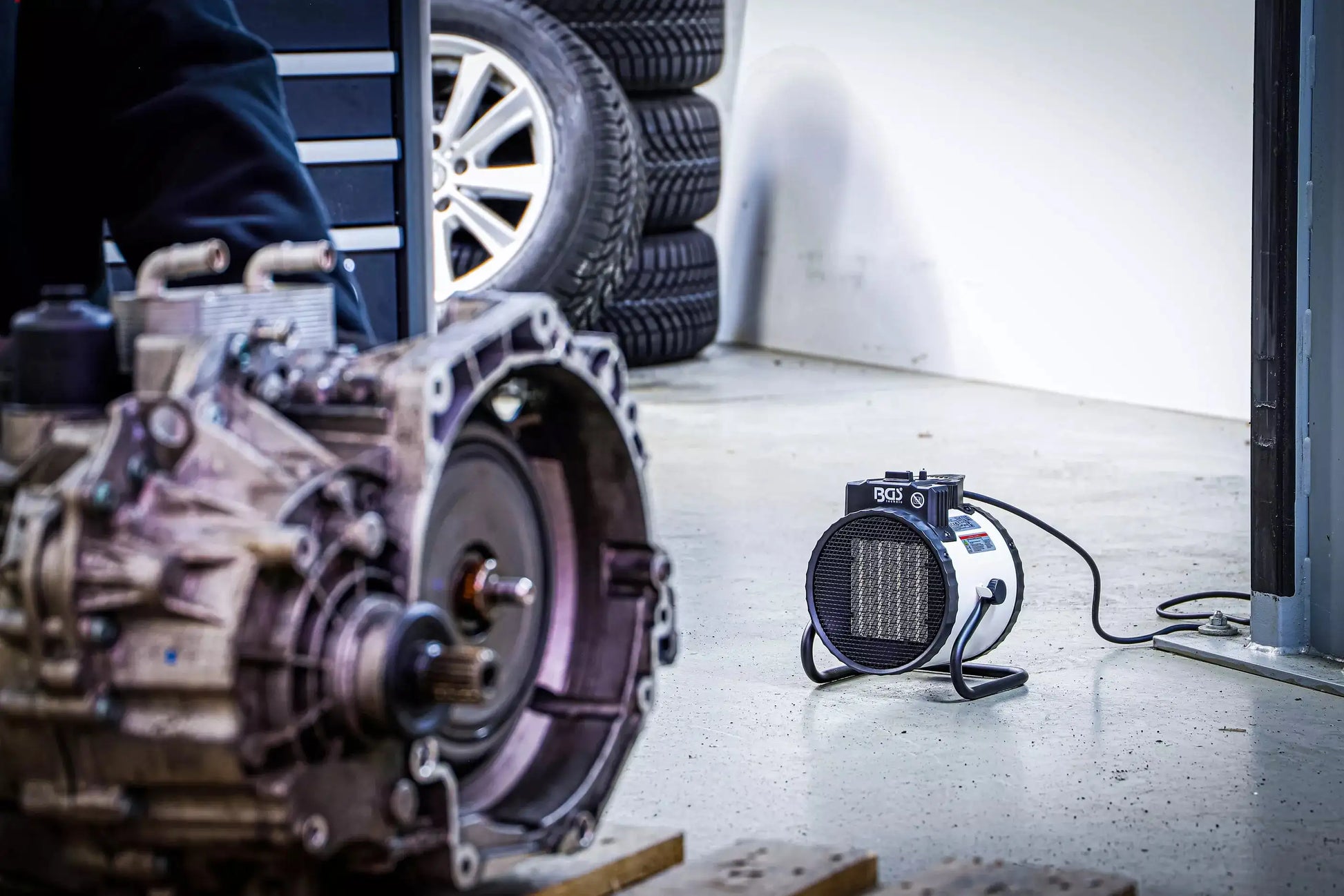 Heizlüfter elektrisch 2 kW BGS in Garage neben Autoteilen. Tragbare Lösung für schnelle und gezielte Raumheizung.