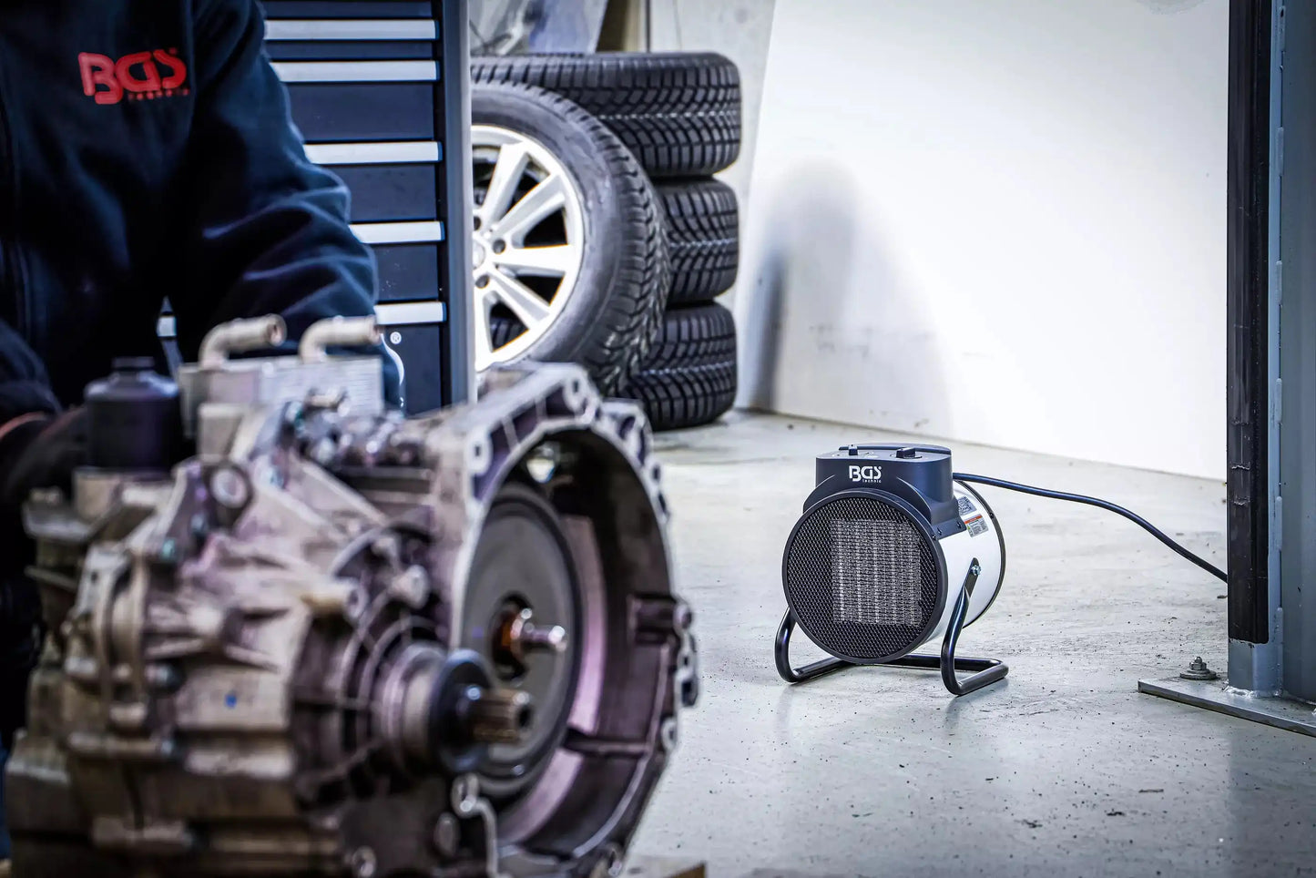 Heizlüfter elektrisch 3 kW von BGS in Autowerkstatt neben Reifen und Getriebe. Effiziente Wärmequelle für kalte Arbeitsbereiche.