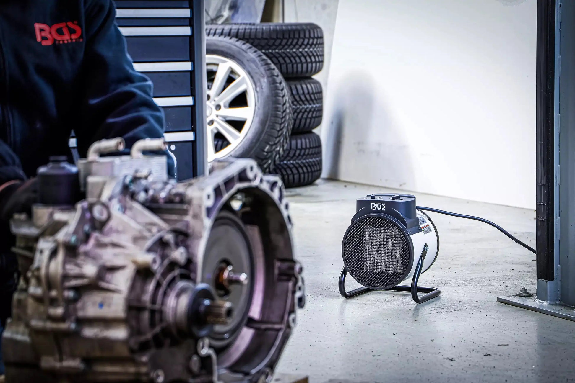 Heizlüfter elektrisch 3 kW von BGS in Autowerkstatt neben Reifen und Getriebe. Effiziente Wärmequelle für kalte Arbeitsbereiche.