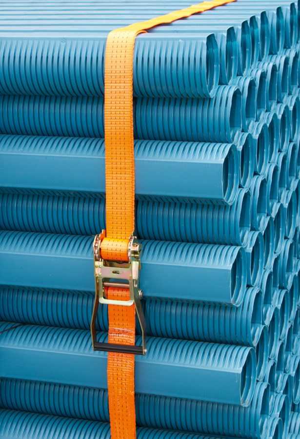 Ratschenzurrgurt mit Spitzhaken 2-teilig 2000 kg orange sichert blaue Kunststoffrohre auf Palette, hohe Zugkraft und UV-Schutz.