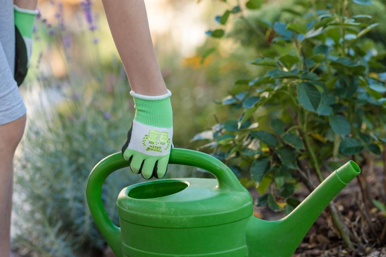 Nachhaltiger THINKGREEN Sprout Kinderhandschuh aus Recycling-Polyester beim Gießen mit einer grünen Gießkanne im Garten.