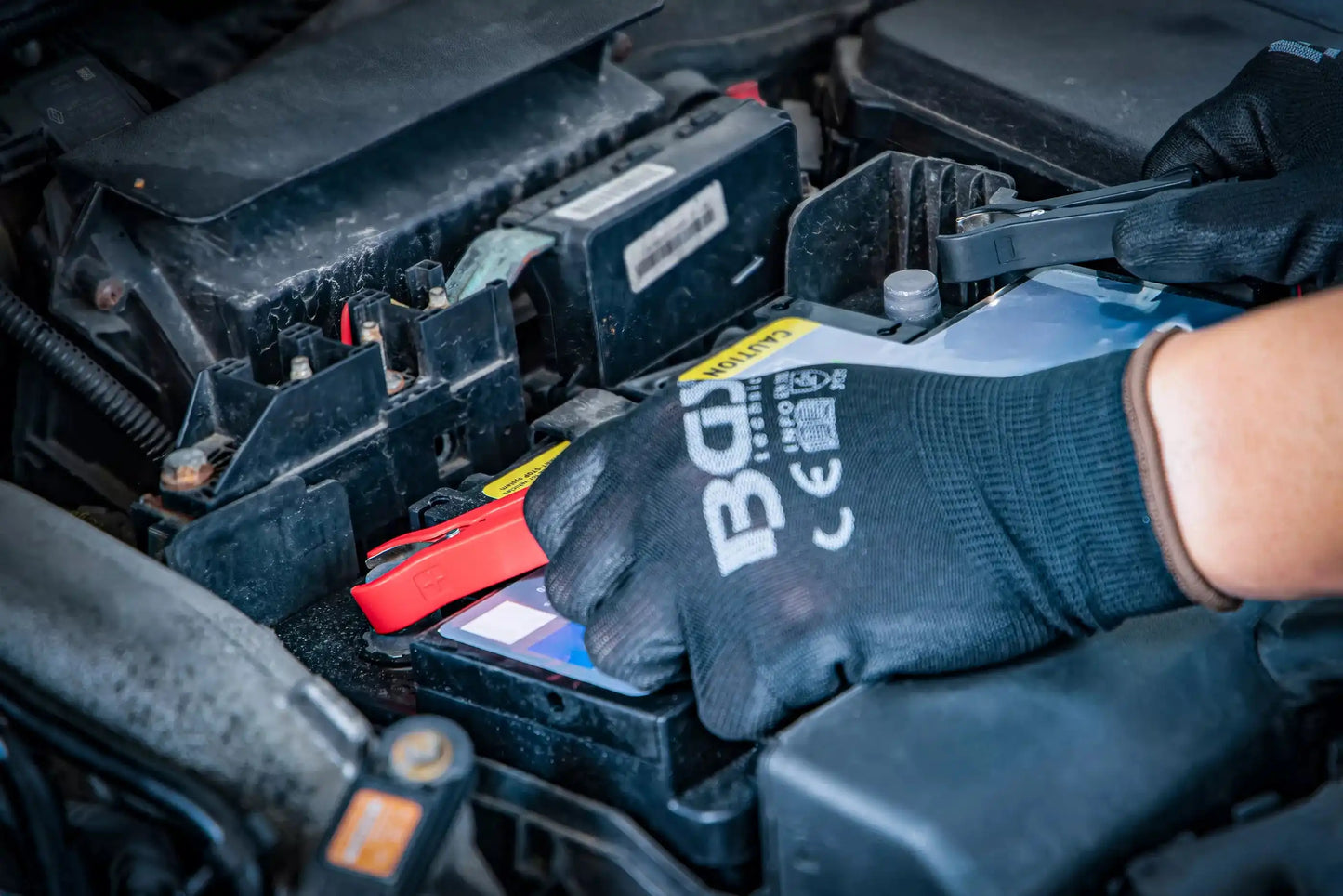 Anschluss des digitalen Batterie-Ladegeräts 6/12 V an eine Autobatterie durch eine Person mit BGS-Handschuhen für sichere Handhabung.
