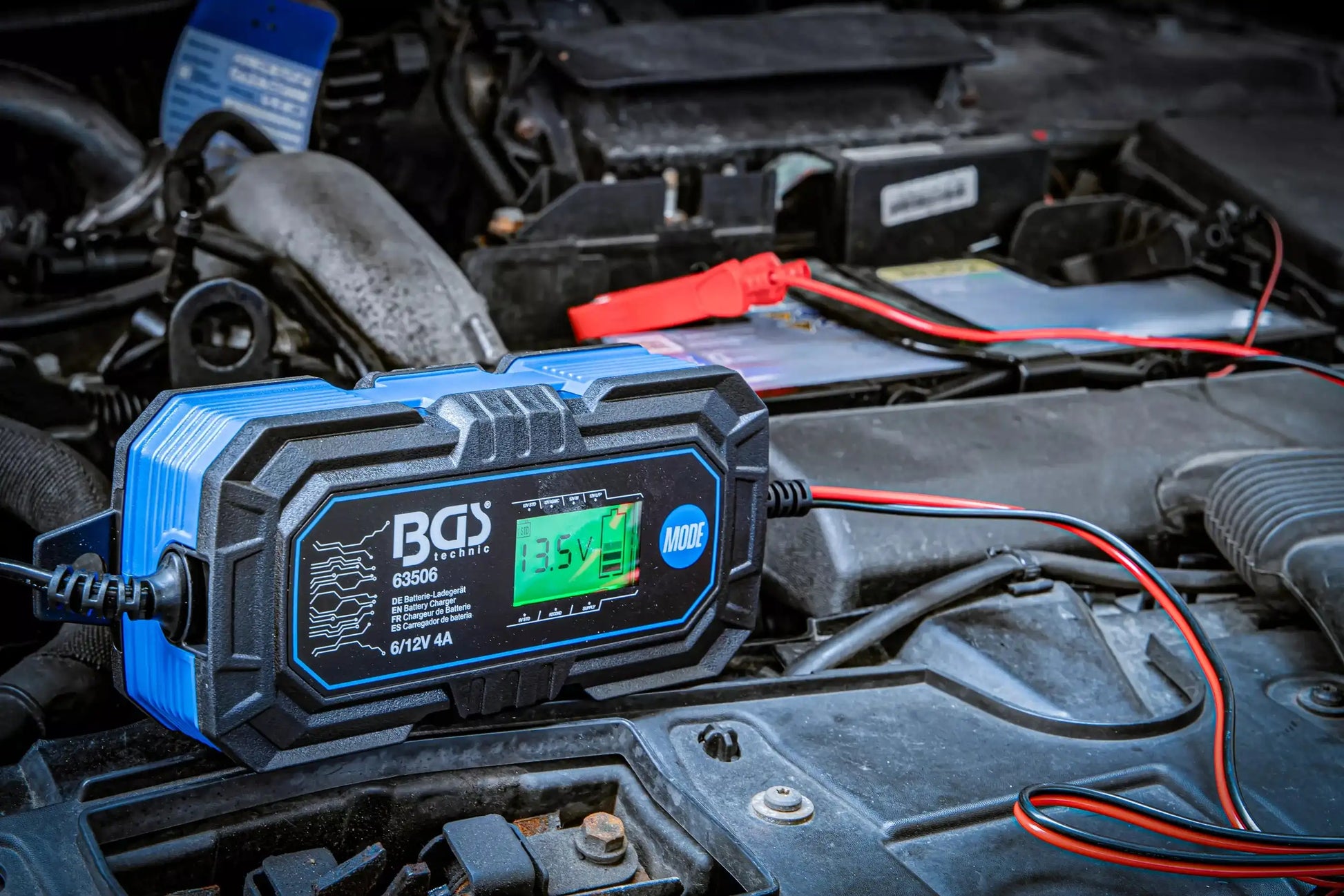 Digitales Batterie-Ladegerät 6/12 V im Einsatz im Motorraum eines Fahrzeugs, zeigt aktuelle Ladespannung auf dem Display an.